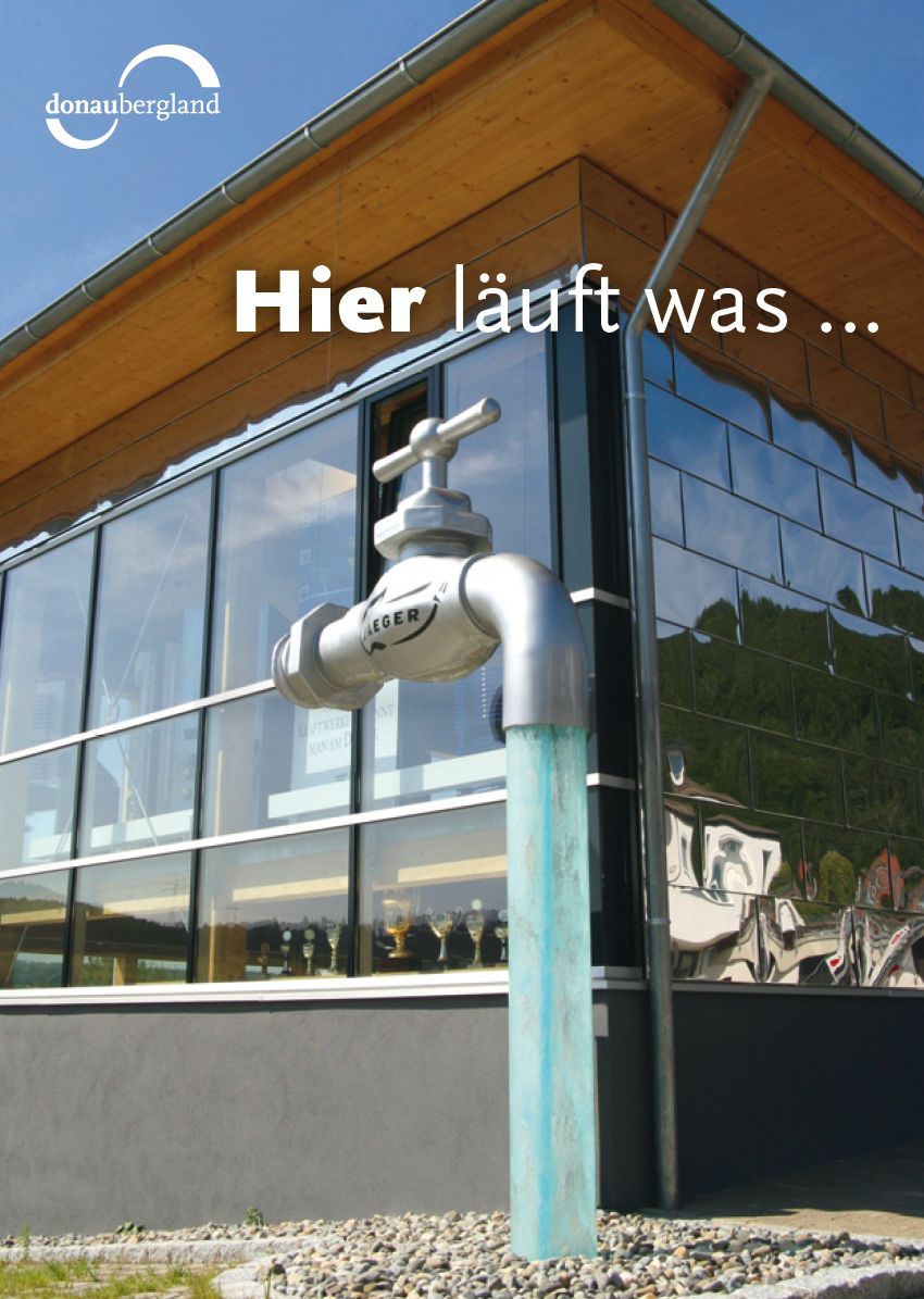 Donaubergland Postkartenmotiv mit großem Wasserhahn vor einem modernen Glasgebäude mit dickem Wasserstrahl