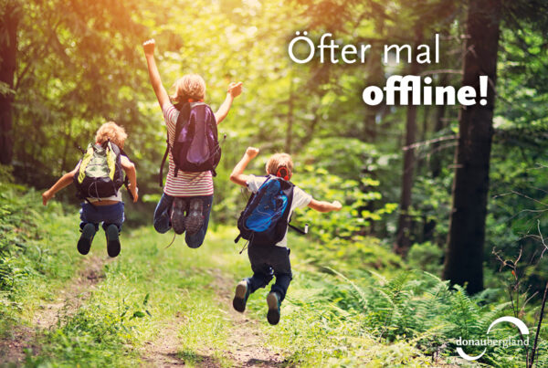 Donaubergland Postkartenmotiv mit drei Kindern, die mit Rucksack auf einem Wanderweg in die Höhe springen.