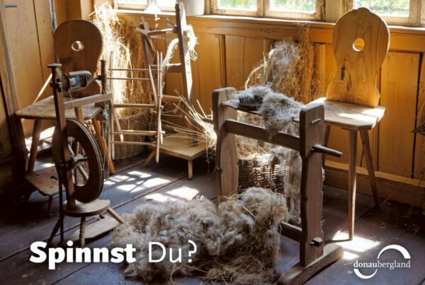 Donaubergland Postkartenmotiv mit Spinnrad und Schafswolle in einem alten Raum und alten Stühlen.